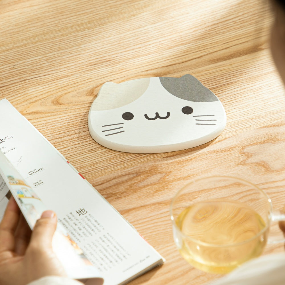 Large diatomaceous earth coaster with cat print on a wooden table with a book and glass of tea.