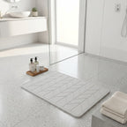 Bathroom with a textured diatomite bath mat on the floor, towels, and toiletries.